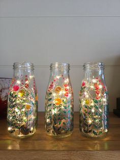 three glass jars with lights in them are sitting on a wooden table next to a vase