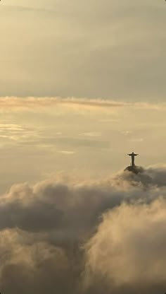 an airplane flying above the clouds with a statue in the middle on it's side