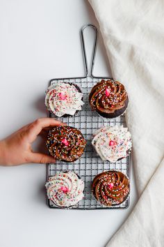 a person reaching for some cupcakes on a cooling rack with sprinkles