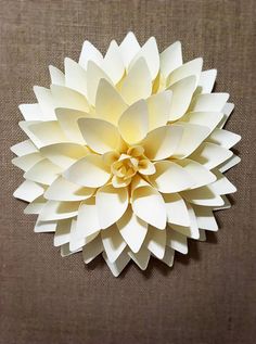 a white paper flower sitting on top of a brown cloth covered table next to a wall