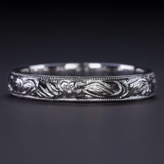 an antique style wedding band with intricate engraving on the sides and center, in white gold