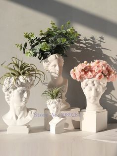 three white vases with flowers and plants in them on top of a table next to a wall