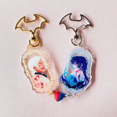 two keychains with anime characters on them sitting next to each other in front of a white background