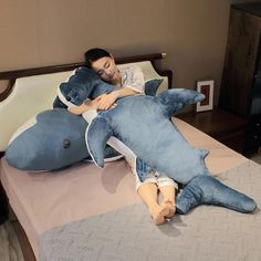 a woman laying on top of a bed next to a giant shark stuffed animal pillow