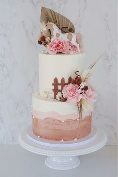 a three tiered cake with pink flowers and feathers on the top is sitting on a plate