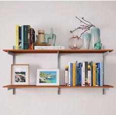 two wooden shelves with books, vases and pictures on them against a white wall