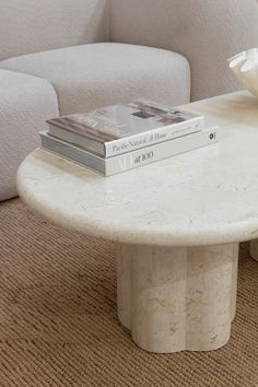 a white table with two books on it and a flower in the middle, sitting next to a couch