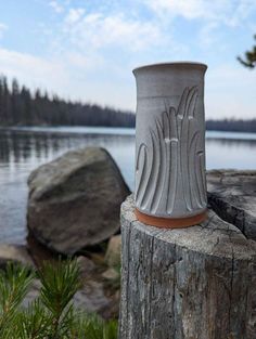 a white vase sitting on top of a wooden post next to a body of water