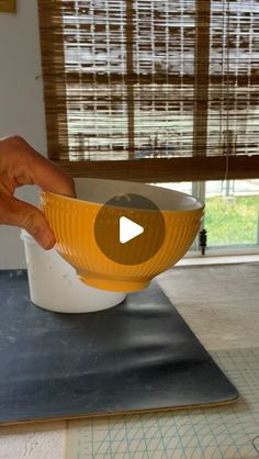 a person is holding a yellow bowl over a black mat on top of a table