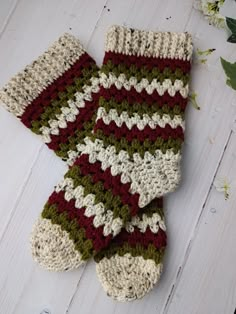 two crocheted mitts sitting on top of a white wooden floor next to flowers