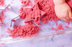 a baby is playing with pink sand and star shaped cookie cutters