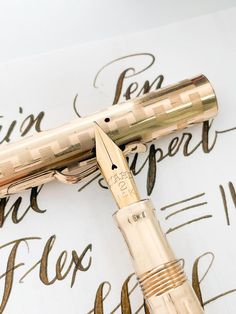 a fountain pen sitting on top of a piece of paper with writing in gold ink