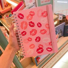 a person holding up a notebook with red lipstick on it in front of a store shelf