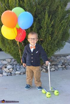 a young boy standing next to some balls with a stick in his hand and two balloons on the ground