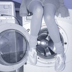 a woman sitting on top of a washing machine next to a dryer with the door open