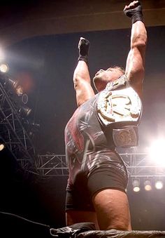 a man standing on top of a wrestling ring holding his hands up in the air