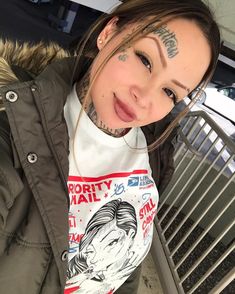 a woman with tattoos on her face and neck standing in front of a grill grate