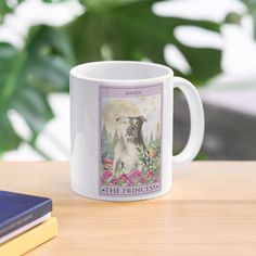 a coffee mug sitting on top of a wooden table next to a book and plant