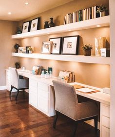 a home office with two desks and bookshelves on the wall above them