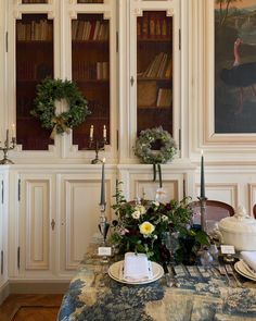 a dining room table is set with flowers and candles for the centerpieces in front of bookshelves