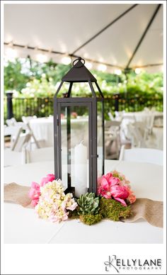 a lantern with flowers on it sitting on top of a table under a white tent