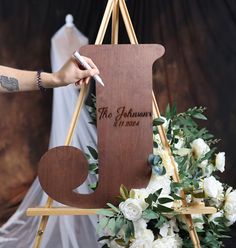 a person writing on a wooden sign with flowers in the foreground and an easel behind it