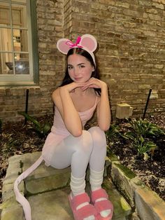 a woman in pink is sitting on steps with her legs crossed and wearing mouse ears