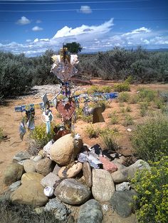 a cross made out of rocks in the middle of a dirt field with trees and bushes behind it