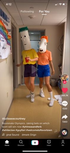 two people are walking down the hallway with paper masks on their heads and one person is wearing shorts