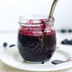 a jar filled with blueberry jam on top of a white plate next to a spoon