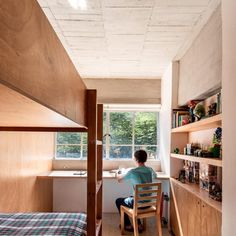 a person sitting on a chair in a room with bunk beds and shelves filled with books