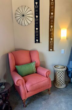 a pink chair sitting in a living room next to a lamp and wall hangings