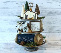 a three tiered christmas tree with ornaments and signs on it's sides, in front of a white wooden background