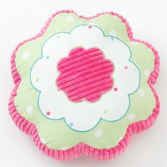 a pink and green flower shaped pillow on a white surface with polka dots around it