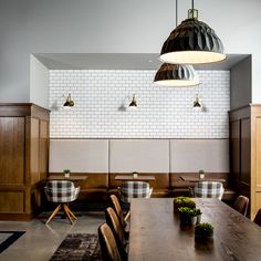 a dining room with wooden tables and chairs next to a white brick wall that has hanging lights above it