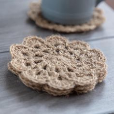 two crocheted coasters sitting on top of a table next to a cup