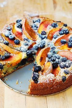 a cake with blueberries and peaches is on a plate next to a slice missing