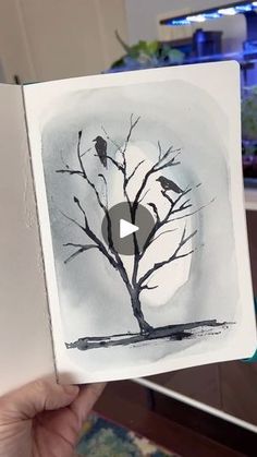 a person holding up an open book with a drawing of a tree and two birds on it