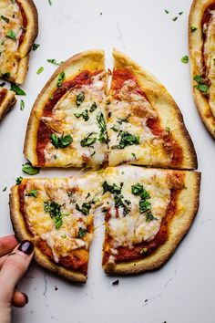 someone is about to cut into four slices of pizza with cheese and herbs on top