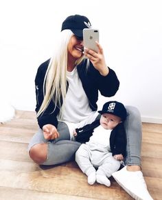 a woman sitting on the floor taking a selfie with her baby and wearing a hat