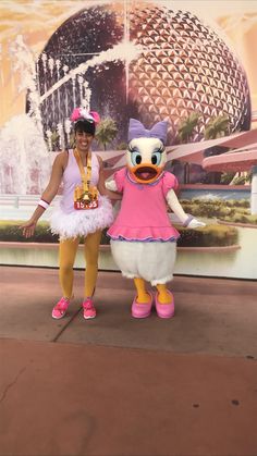 two women standing next to each other in front of a disney world character sign and fountain