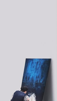 a man sitting on top of a white chair next to a blue and black painting