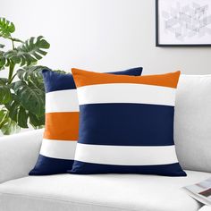 two blue and orange striped pillows on a white couch next to a potted plant