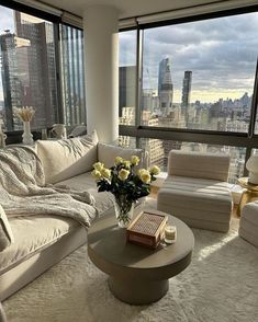 a living room filled with furniture and large windows overlooking the cityscape in the distance