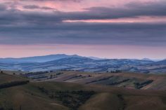 the rolling hills are covered in green grass and under a cloudy sky with pink clouds