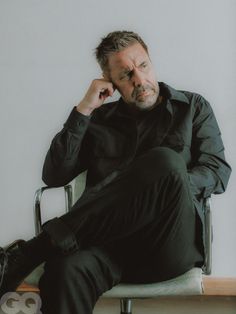 a man sitting in a chair holding his hand to his ear and looking at the camera