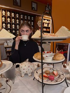 a woman is sitting at a table with tea and pastries on it while holding a cup in her hand