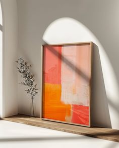 an orange and pink painting sitting on top of a wooden shelf next to a vase