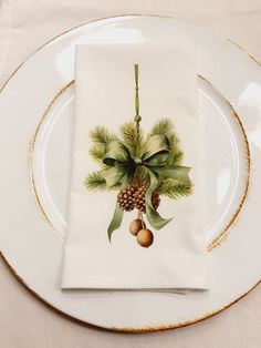 a white plate topped with a napkin covered in pine cones and greenery on top of it