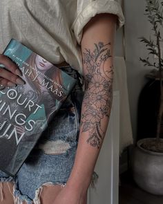 a woman holding a book in her right arm and tattoos on her left arm,